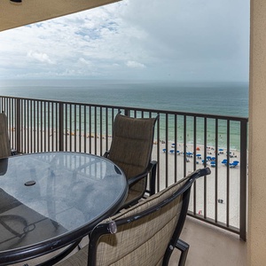 A round table with four chairs overlooks the beach front, providing a perfect spot to enjoy the coastal view