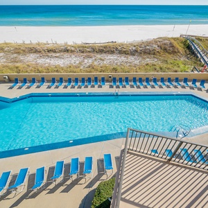 The vibrant pool area features numerous lounge chairs and offers a direct view of the beach and tranquil blue waters