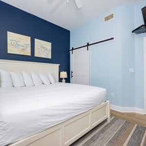 Stylish guest bedroom features a king bed, coastal artwork, and a mounted TV, creating a relaxing retreat
