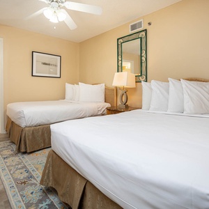 Two double beds with plush white bedding, a decorative lamp, and a view into the bathroom create a welcoming guest bedroom