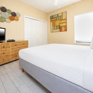 This cozy bedroom features a stylish wicker dresser, a flat-screen TV, and colorful wall art, perfect for relaxation