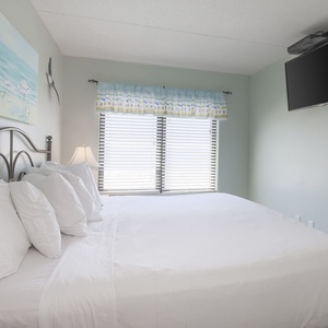 This inviting bedroom features a comfortable bed, natural light and a beach view from large windows, and coastal decor