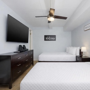 This guest room features two double beds, a large TV, and a welcoming atmosphere, perfect for relaxation