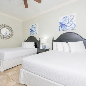 Cheerful guest bedroom featuring two cozy queen beds, elegant decor, and charming artwork on the walls