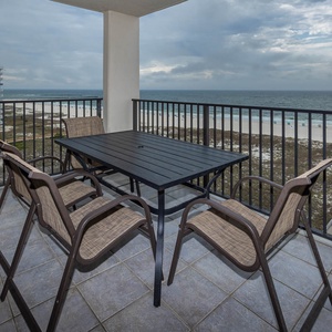 Balcony with a dining table and chairs offers a relaxing spot to enjoy views of the beach and gentle waves below