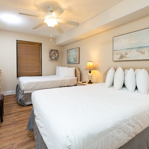 A cozy guest bedroom features two double beds, a flat-screen TV, and beach-themed artwork, creating a relaxing atmosphere