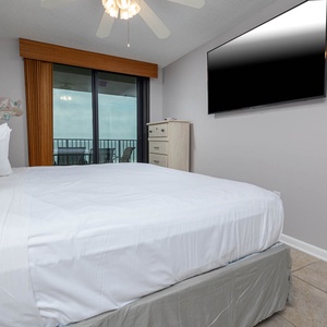 The master bedroom features a plush king bed, wall-mounted TV, and sliding glass doors leading to a balcony with beach views