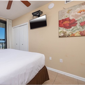Cozy guest bedroom featuring a comfortable queen bed, a mounted TV, and a vibrant floral artwork