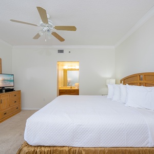 Spacious master bedroom features a king bed with plush linens, warm gold tones, and an adjoining bathroom for convenience