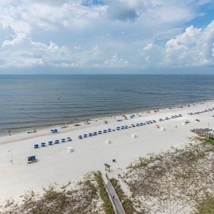Wide stretch of white sand beach lined with blue umbrellas and gentle waves under a bright sky