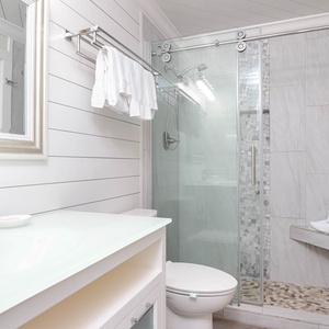 The bathroom features a glass-enclosed walk-in shower, a sleek vanity with a lighted mirror, and neatly arranged towels