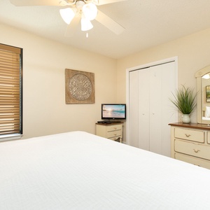 Spacious guest bedroom features a large king bed adorned with fluffy pillows, a flat-screen TV, and a serene beach painting