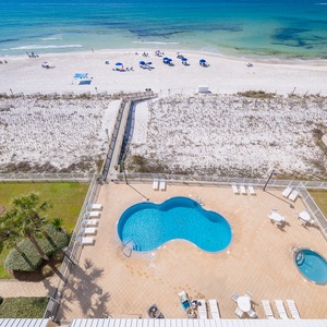 A shimmering pool rests below as you gaze across the dune path to white beach and calm waves