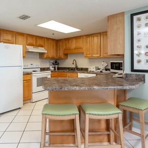 The fully-equipped kitchen features warm wood cabinetry, a stylish countertop, and a breakfast bar with green-topped stools