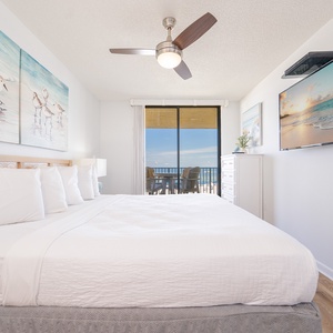 Bright and airy master suite featuring a king bed, wall-mounted TV, and a balcony view overlooking the beach
