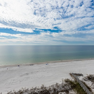 A serene view of a tranquil beach with white sand and gentle waves under a partly blue sky, inviting relaxation and leisure