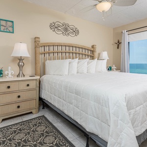 This inviting bedroom features a plush bed and stunning beachfront views through large windows, perfect for relaxation