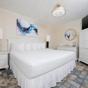 Bright bedroom featuring a large king bed with white linens, a mounted TV, and stylish decor against a colorful tile floor