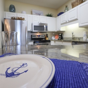 A stylish kitchen features white cabinetry, marbled countertops, and nautical-themed decor, perfect for meal prep