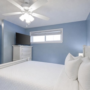 The master suite features soft blue walls, a queen bed, and a TV, creating a serene retreat for relaxation