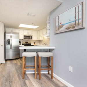 The bright kitchen features sleek appliances, a breakfast bar with seating, and coastal art enhancing the inviting atmosphere