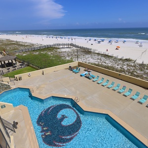 Relax by the inviting pool with a vibrant design, overlooking the serene beach and colorful umbrellas in the distance
