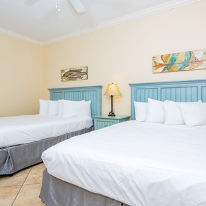 The guest bedroom features two comfortable queen beds with light blue headboards, complemented by beach decor and warm tones