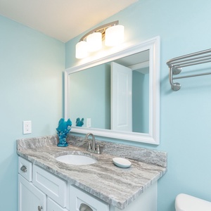 The guest bathroom features a light blue wall, stylish vanity with a granite countertop, and decorative accents in turquoise