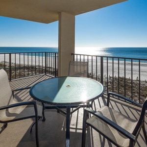 Balcony featuring a patio table with four chairs, offering a tranquil view of the shimmering beachfront and blue waters