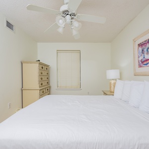 Bright and airy guest bedroom featuring a queen bed, decorative artwork, and a charming dresser with a lamp for a cozy vibe