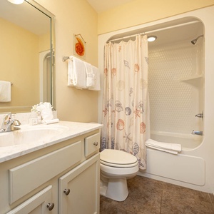 This bathroom features a clean design with a marble countertop, a shower curtain adorned with seashells, and fresh towels