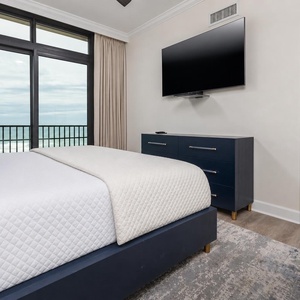 This bedroom features a large window with a beachfront view, a mounted TV, and stylish blue accents for a relaxing stay