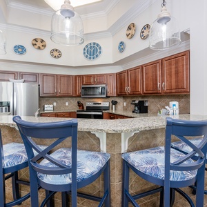 Kitchen featuring stainless appliances, granite countertops, and stylish bar seating with tropical-patterned cushions