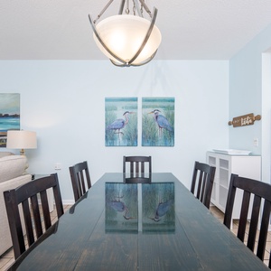 Dining area features a dark wood table surrounded by chairs, with coastal artwork