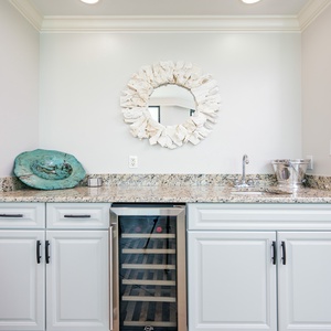 Enjoy refreshments at the sleek wet bar area, featuring a stylish wine cooler and coastal-inspired decor