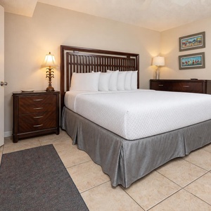 The cozy bedroom features a king bed with crisp white linens, warm lighting, and tasteful artwork on the walls