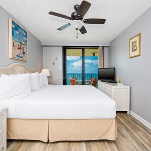 Brightly decorated master bedroom featuring a king bed, a TV, and the balcony with a view of the beach and balcony access