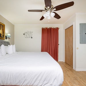 The bedroom features a plush king bed with white linens, a colorful artwork above, and warm curtains adding a welcoming touch