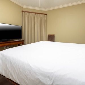 Unwind in this inviting guest bedroom featuring a plush queen bed, a large TV, and soft lighting for a restful atmosphere