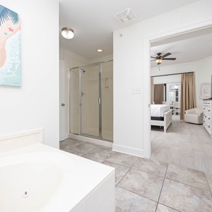 This bathroom features a relaxing tub, a glass walk-in shower, and a view into the inviting bedroom with a TV and light decor