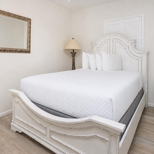 Sleep soundly in this charming guest bedroom featuring a plush queen bed, decorative lamp, and elegant mirror