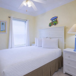 Cozy guest bedroom featuring a queen bed, light yellow walls, and a charming beach decor accentuated by a blue lamp
