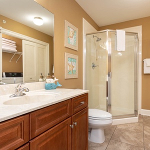 The extra bath features a walk-in shower, elegant cabinetry, beach décor, and laundry closet with a washer and dryer area