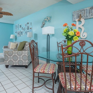 The living area features a vibrant blue wall, comfortable seating, and a lovely beach view through the balcony doors