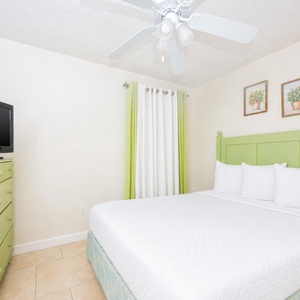 This cheerful guest bedroom features a green accent wall, a TV, and light-colored bedding, creating a refreshing atmosphere