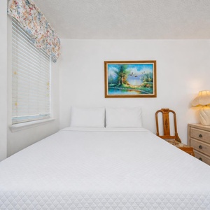 The guest bedroom features a bed with elegant bedding, a charming lamp, and a scenic artwork above, creating a serene retreat