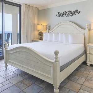 Master bedroom features a king bed, elegant decor, and sliding doors opening to a balcony with a beautiful beach view