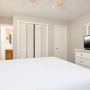 Relax in this guest bedroom featuring a queen bed, a TV, and stylish white furniture for a cozy retreat