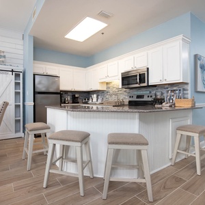 Bright kitchen area features white cabinetry, a granite countertop, and a breakfast bar with four stools for casual dining