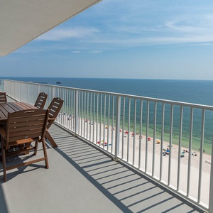 This spacious balcony features a wooden dining set with stunning views of the beach and vibrant umbrellas along the shore